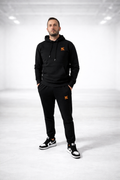 Homme portant l'ensemble noir causal de la marque FL-FIT avec le logo brodée FL de couleur orange un style décontracté 