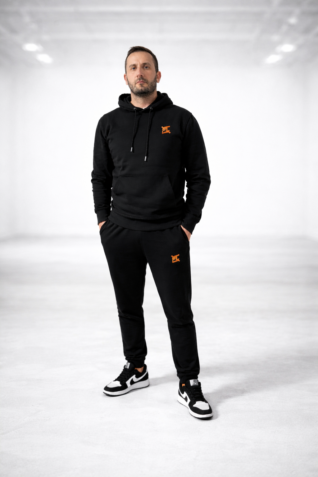 Homme portant l'ensemble noir causal de la marque FL-FIT avec le logo brodée FL de couleur orange un style décontracté 